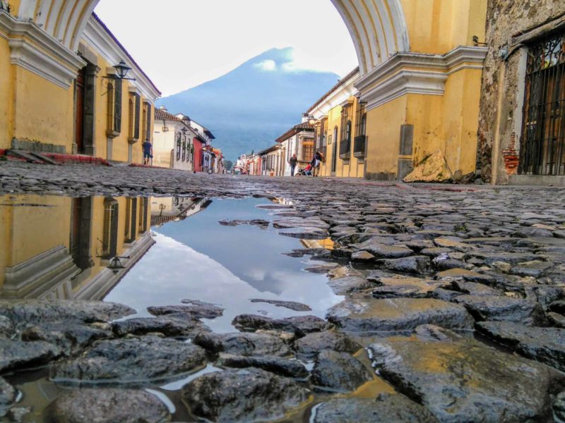 Cobblestones in Antigua Guatemala looking through a colonial archway to a volcano wreathed in morning mist