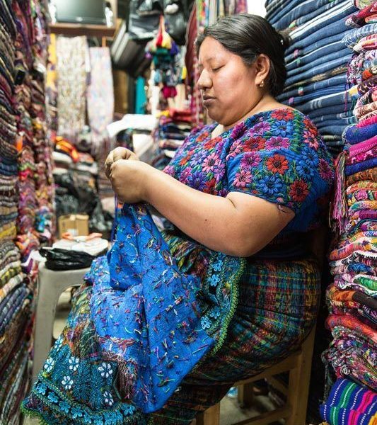 A woman sews at her textile stall in Antigua Guatemala, a city you can visit can visit on a women travel group tour