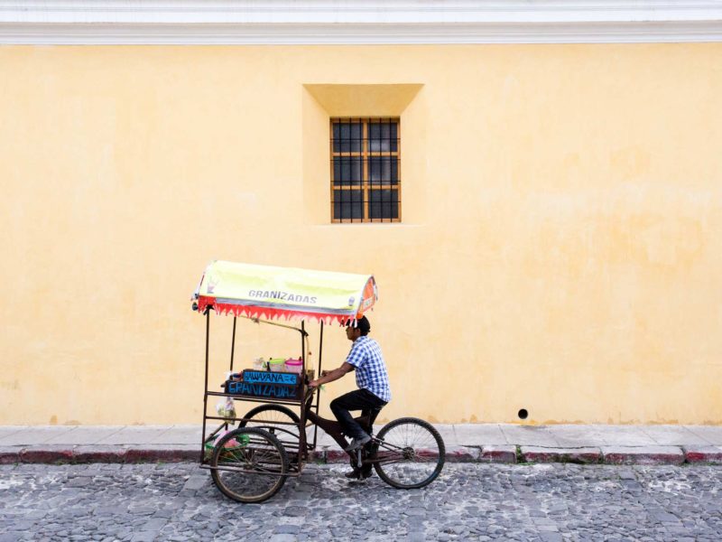 A local cycles down a cobbled street in the pretty colonial city of Antigua Guatemala, a city you can visit can visit on a women travel group tour