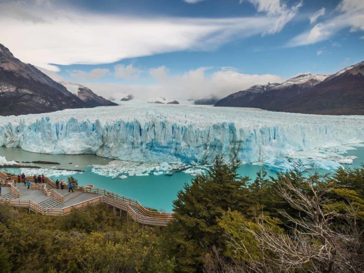 Views of the impressive snout of the Perito Moreno Glacier in Los Glaciares National Park with people stood on boardwalks beneath it. 