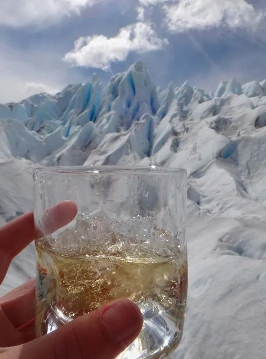 A whisky with ice taken from El Perito Moreno Glacier being held up in front of the glacier itself