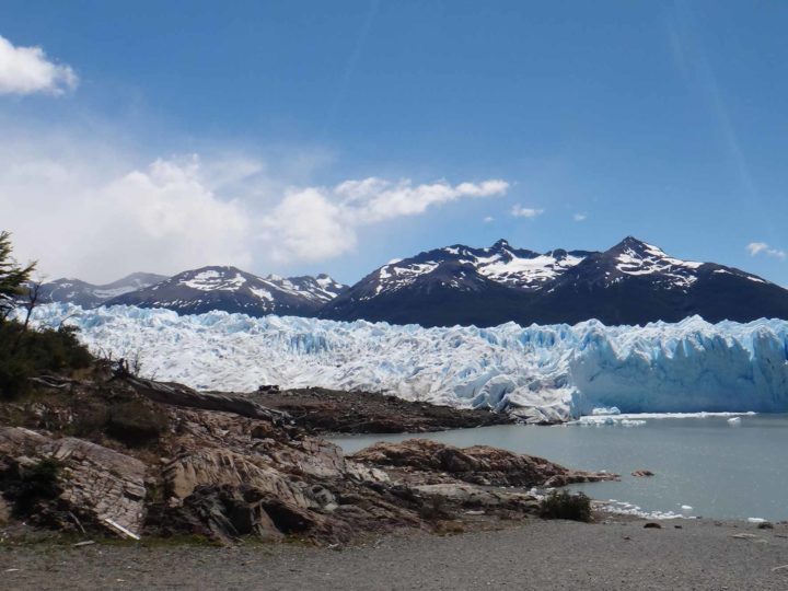 A beach and rocks on Lago Argentina with the wall of the El Perito Moreno Glacier, Argentina in the background