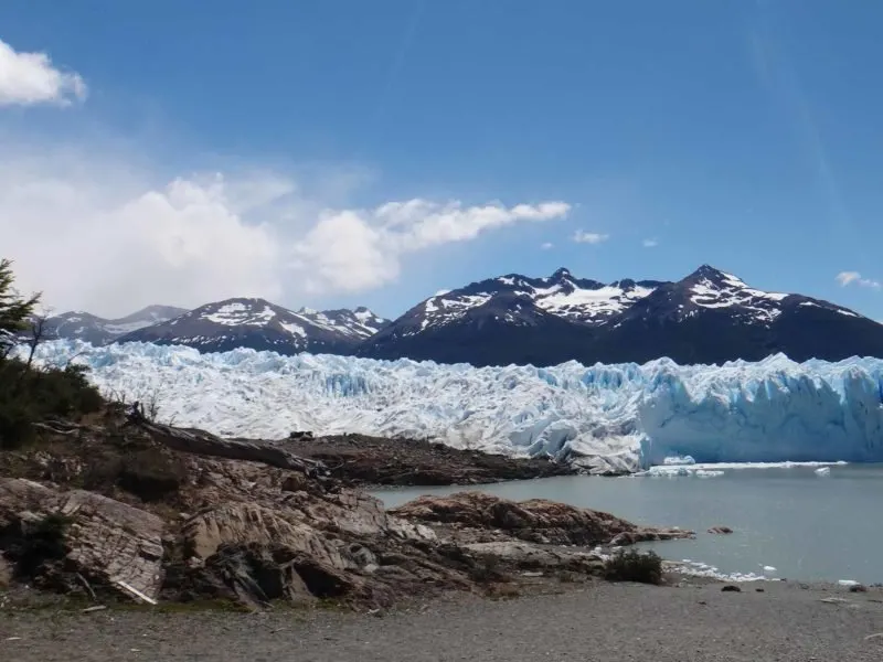 A beach and rocks on Lago Argentina with the wall of the El Perito Moreno Glacier, Argentina in the background
