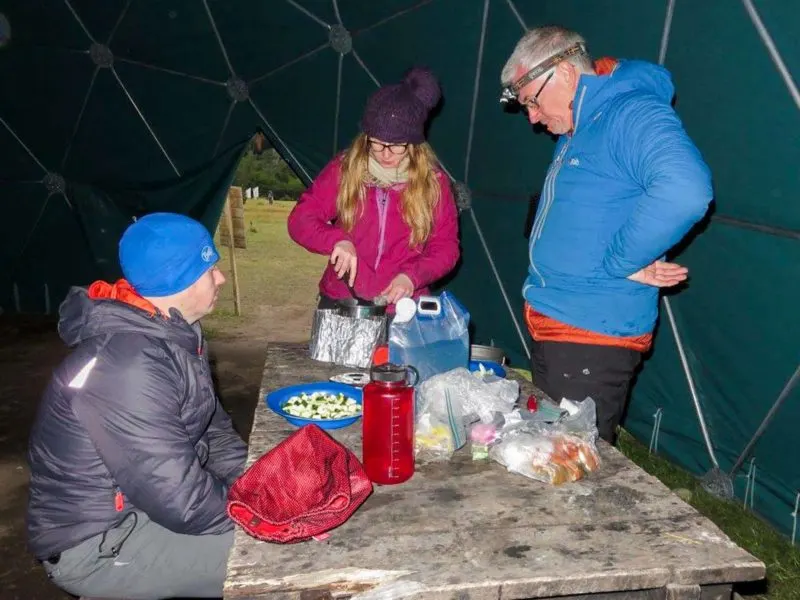 Three hikers in a geodesic dome in Campamento Dickson cook over camping stoves while hiking the O Circuit in Torres del Paine National Park, Patagonia