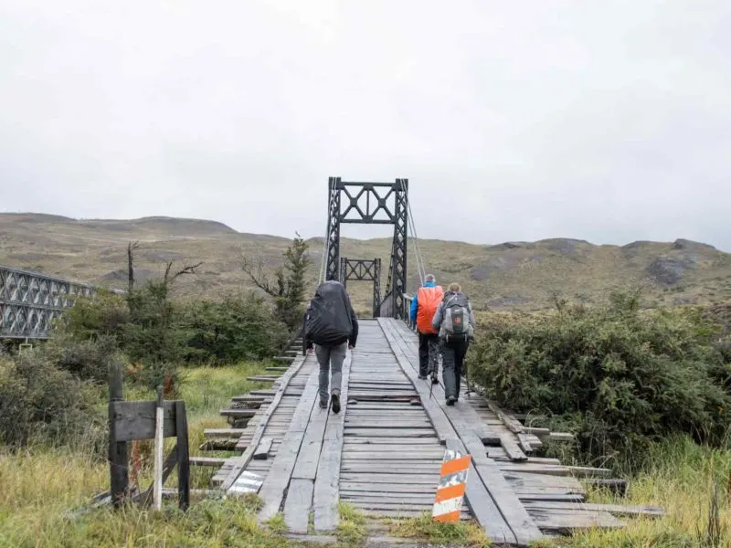 Three hikers cross a bridge while hiking the O Circuit in Torres del Paine National Park, Patagonia