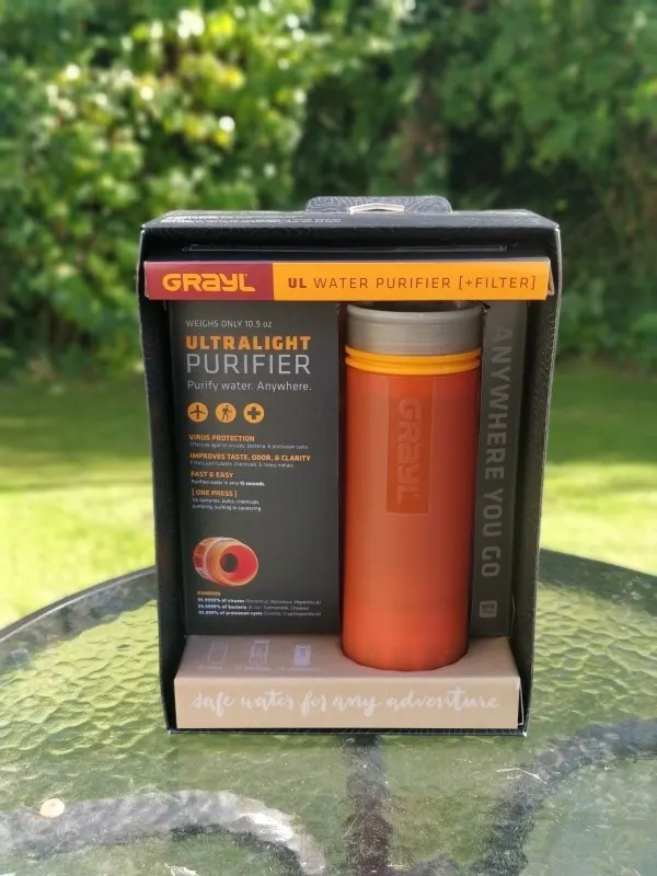 An orange Grayl Geopress travel water filter in its packaging in a natural setting