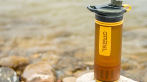 An orange Grayl Geopress travel water filter sits on a rock in front of a river