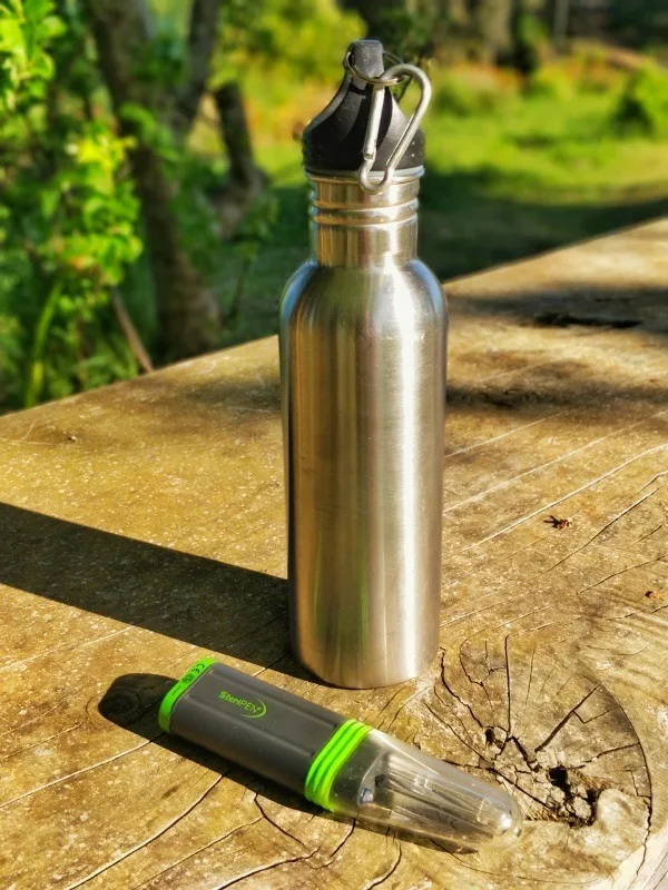 A Steripen water purifier sits next to a silver metal water bottle on a rustic table