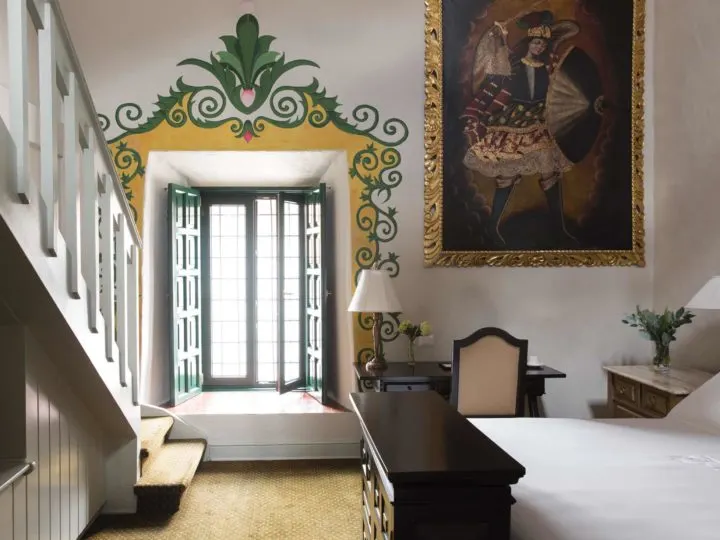 A simply furnished Cuzco hotel room with elaborate painted decoration around the window