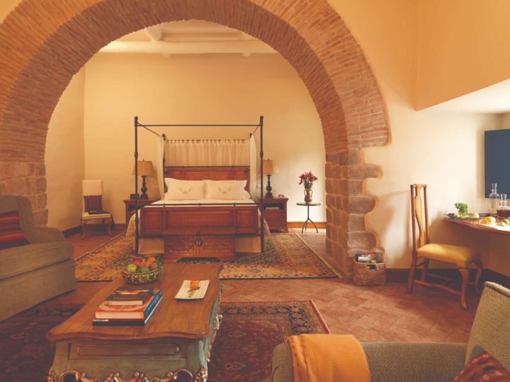 Looking through a strong brick arch toward a four-poster bed in a Cuzco hotel room.