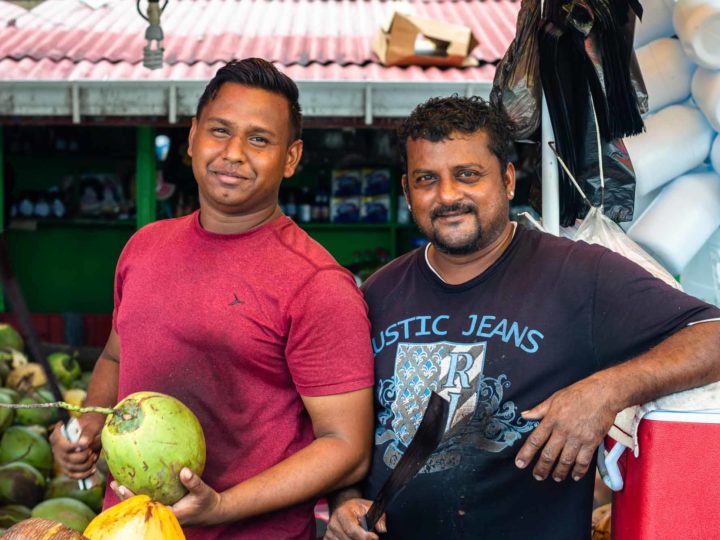 Two men stand in front of their coconut stand in Bourda Market, Guyana in South America