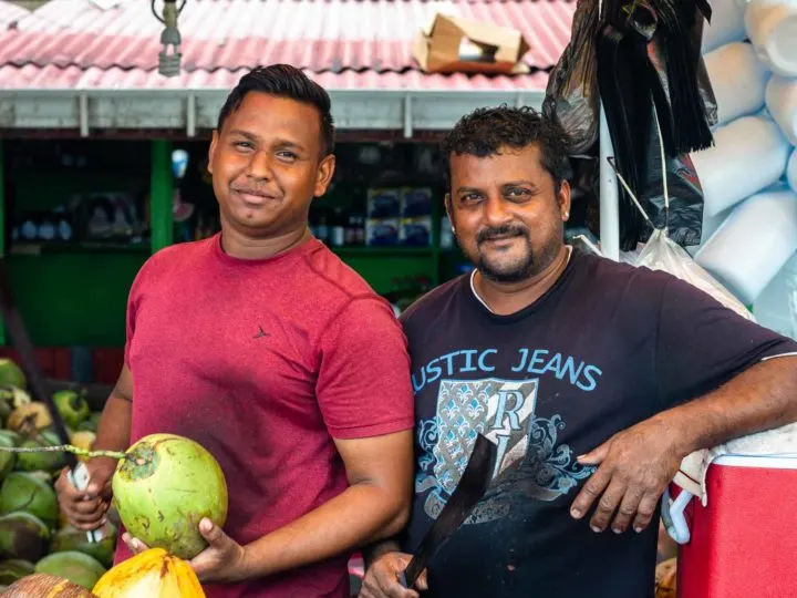 Two men stand in front of their coconut stand in Bourda Market, Guyana in South America