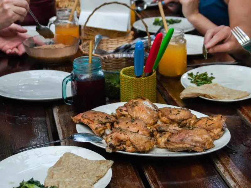 Tourists in Guyana gather around a rustic table and chat over pieces of chicken.