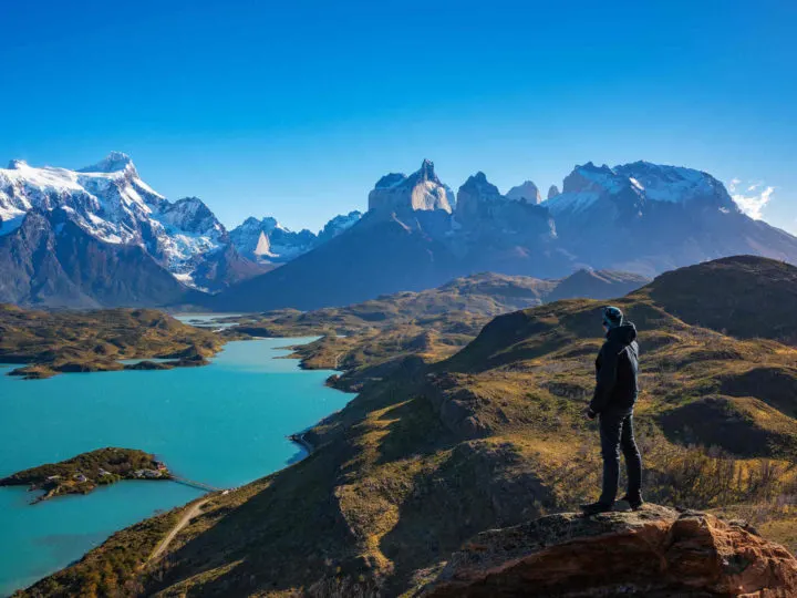 A man stands at Mirador Condor on a day hike in Torres del Paine, looking across Lago Pehoe and the mountains of the Cordillera Paine beyond