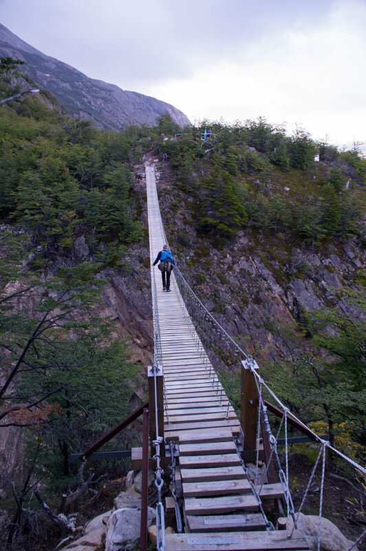A hiker stands on a wooden hanging bridge on a day hike in Torres del Paine National Park