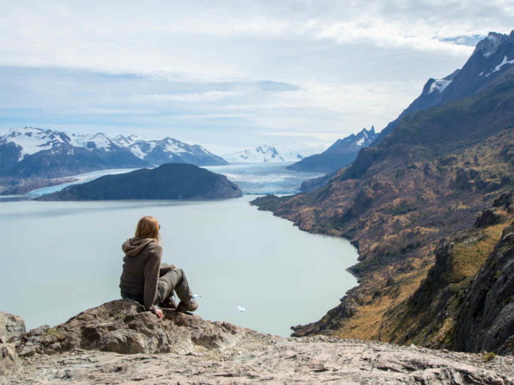 A hiker sits on a rock at the Quebrada de los Vientos (Windy Gorge) viewpoint in Torres del Paine National Park with Lago Grey and Glaciar Grey in the background