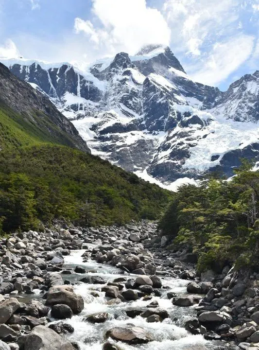 A river runs across rocks with a snow-dusted mountain above it in Valle Frances in Torres del Paine National Park, Patagonia