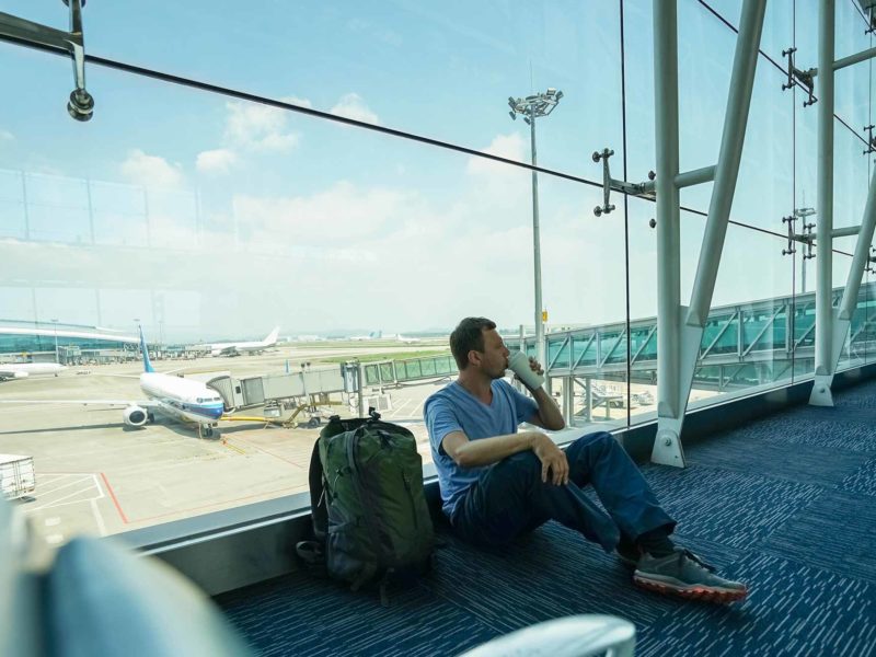 A traveller sits on the floor in an airport while drinking from a coffee cup