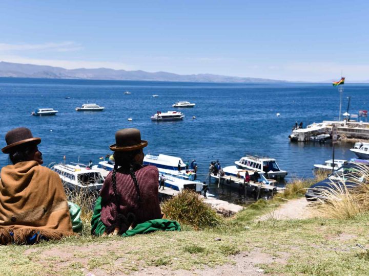 Two cholitas in traditional Andean dress sit on a hill overlooking Lake Titicaca on Isla del Sol
