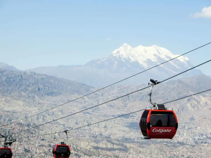 Three red cable cars on the red line in La Paz against a backdrop of the city and Illimani beyond