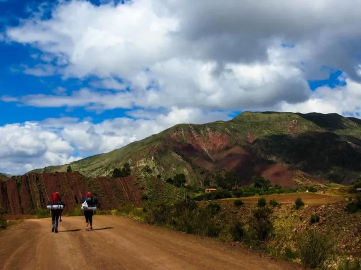 Two hikers walking along a path next to rainbow coloured rock in the Maragua Crater near Sucre, Bolivia