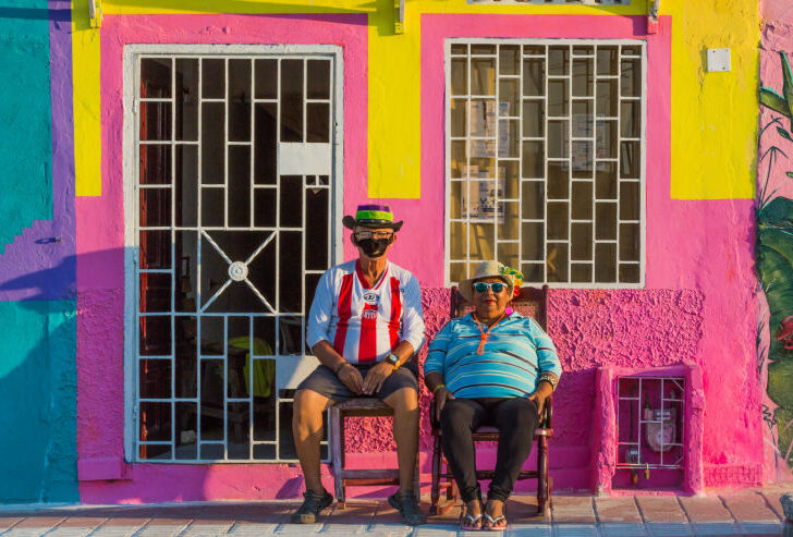 Two people sit outside a colourful building in the town of Baranquilla, a day trip away from Cartagena in Colombia