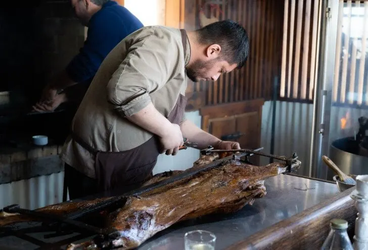 A chef preparing cordero al palo or roast lamb, a staple Patagonian dish cooked over an open fire.