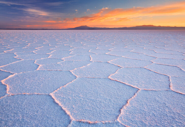 Sunrise lights up the sky behind the salt flats of the Salar de Uyuni in Bolivia, one of the cheapest countries to visit in South America