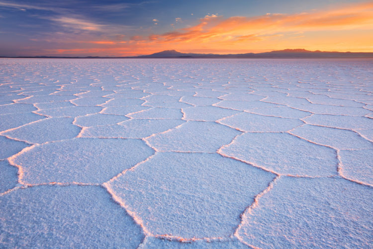 Sunrise lights up the sky behind the salt flats of the Salar de Uyuni in Bolivia, one of the cheapest countries to visit in South America
