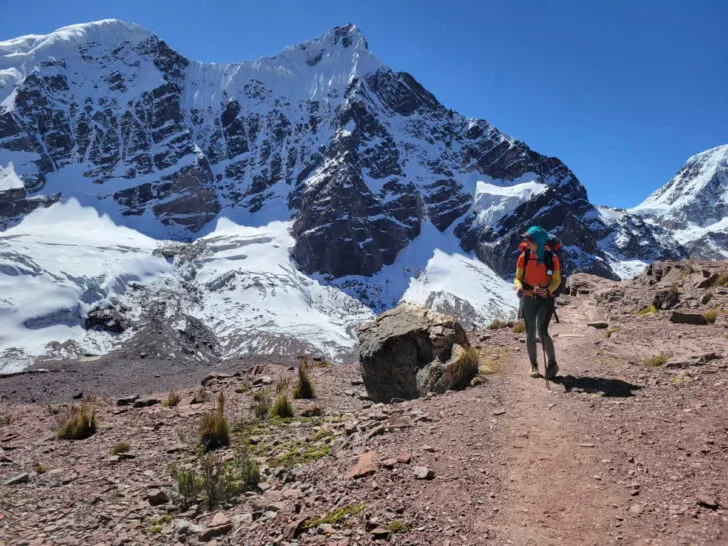 Snow-capped mountains and a hiker in the Ausangate trek, one of the best hikes in Peru.